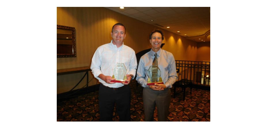 two gentleman smiling while holding awards