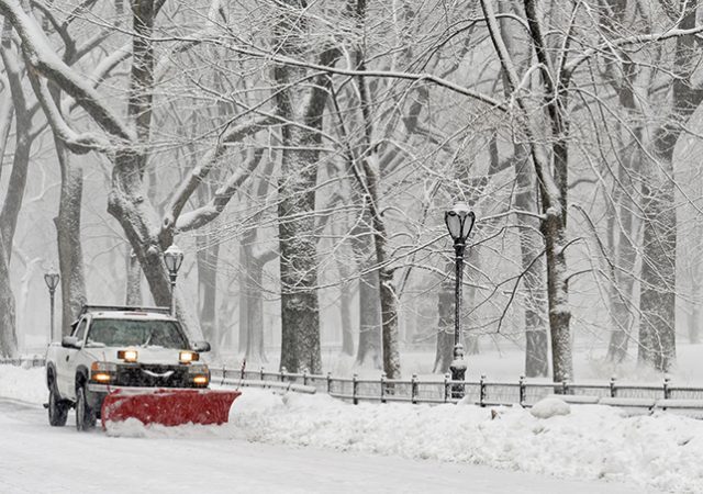 Truck with snowplow clearing road during snowstorm
