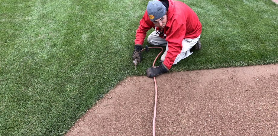man using air to blow infield mix out of grass edge
