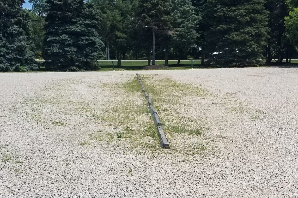 Gravel parking lot with weeds growing around line of parking stops