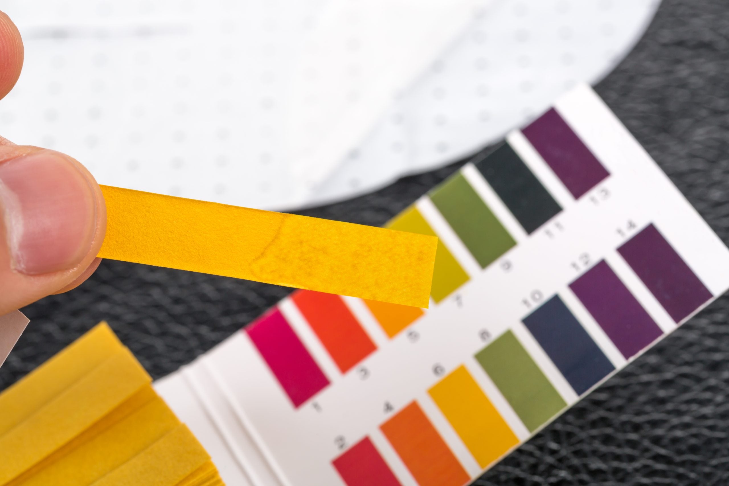 Hand holding pH indicator comparing color to scale. Test the pH