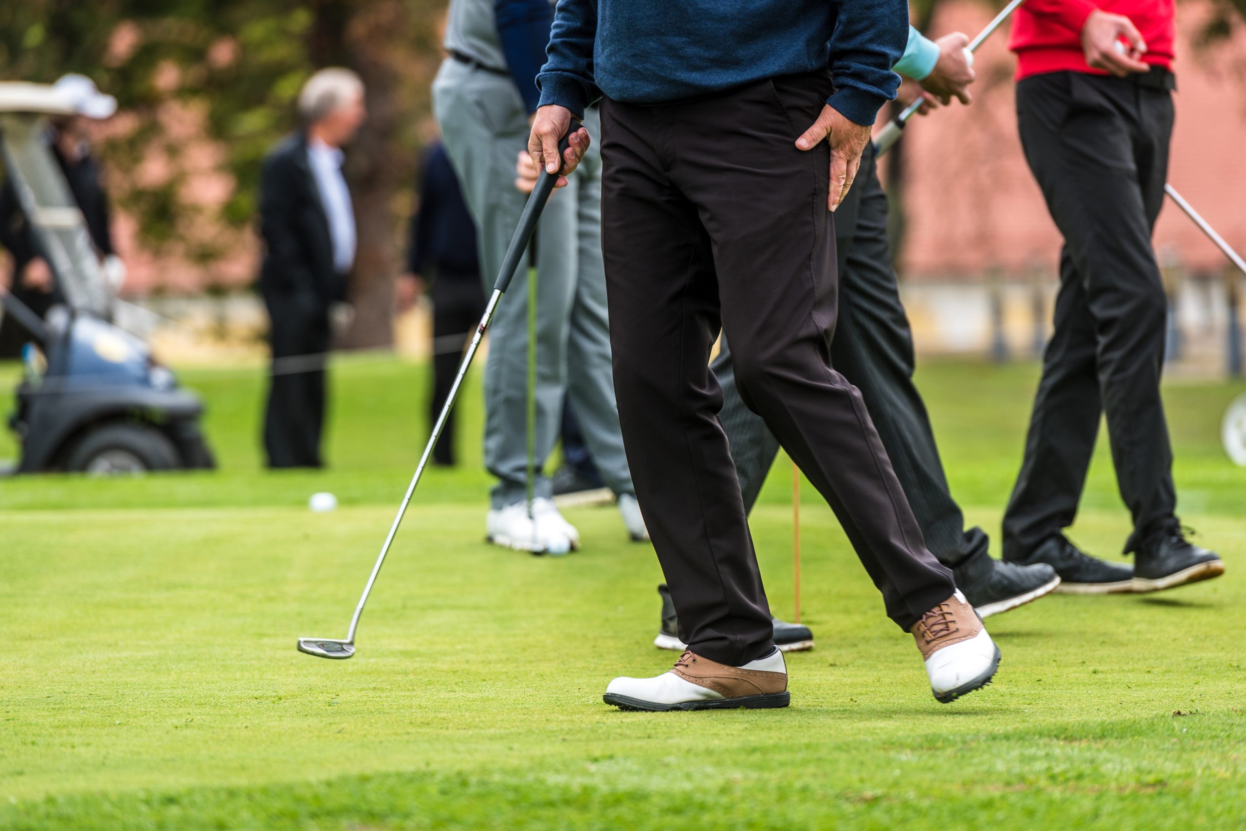 Golfer legs at golf tournament practice swing with golf club. Golf players on green lawn putting golf ball in the hole. Golfing competition or tournament.