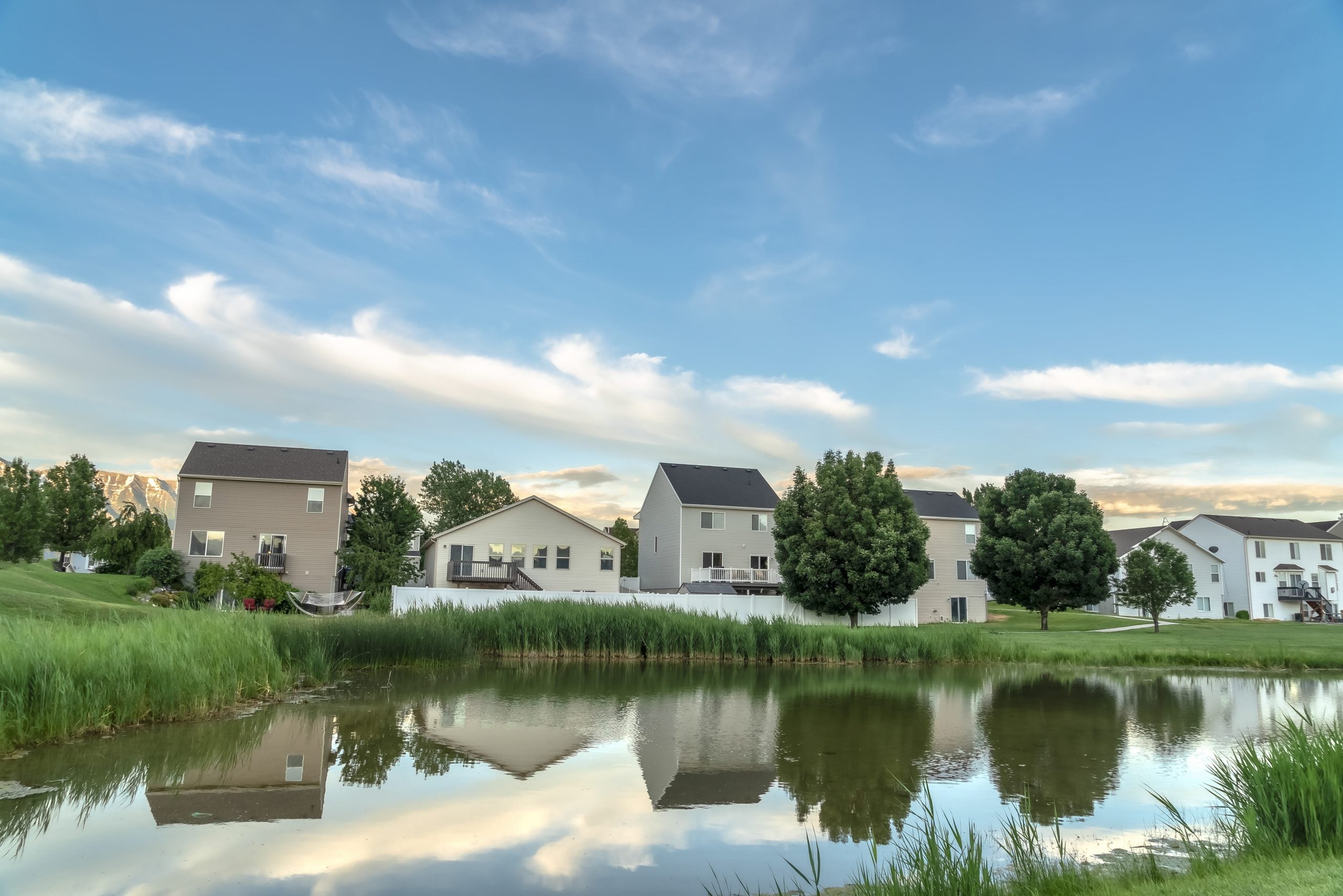 Scenic suburban landscape with homes and cloudy sky reflected on a shiny pond