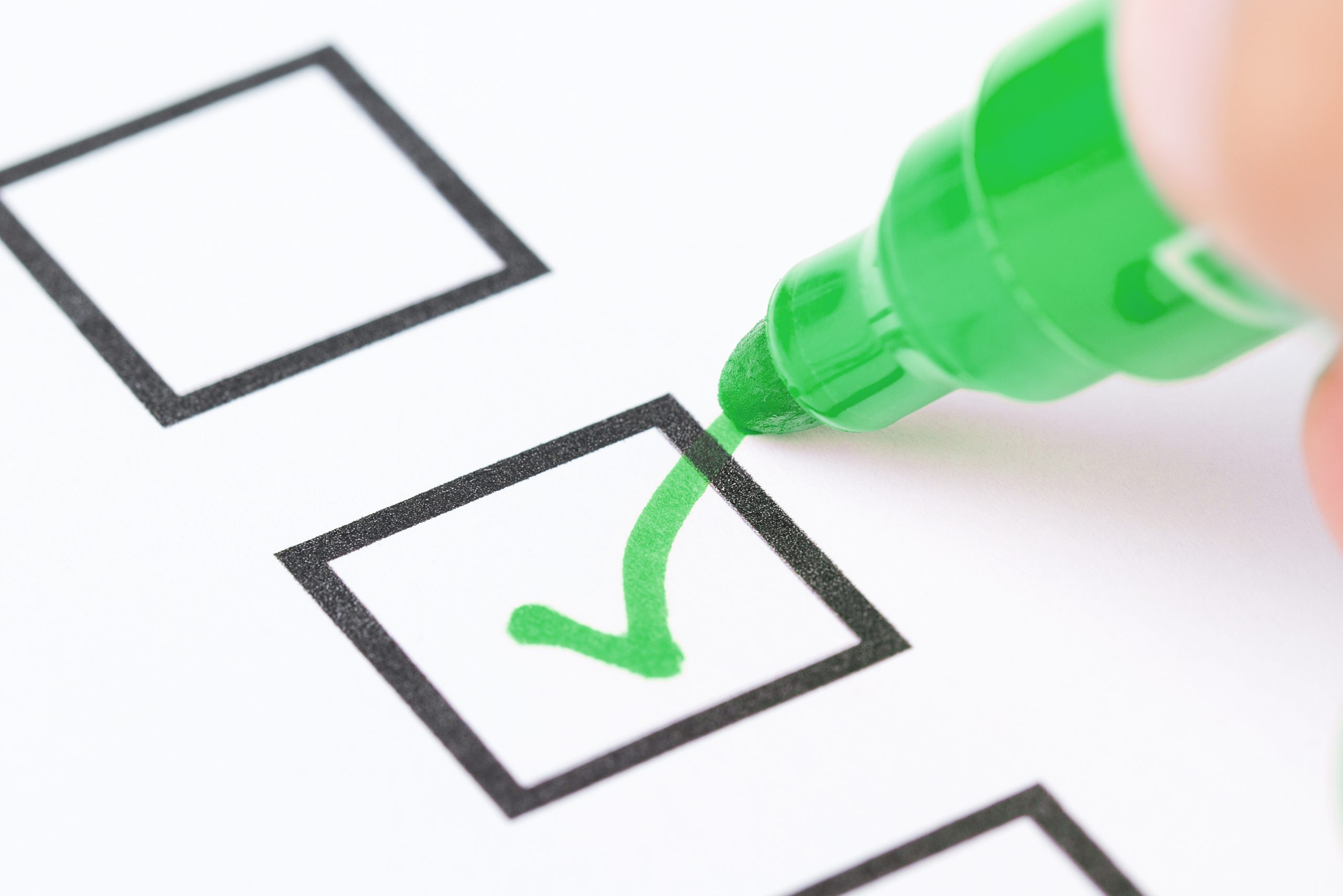 Macro shot of human hand drawing green check mark in checklist