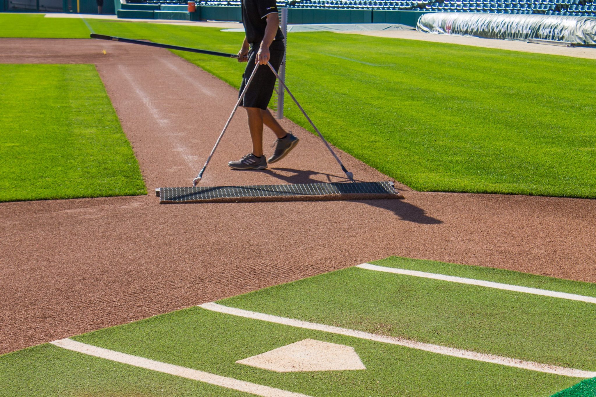 close up of home plate and gentleman leveling the dirt in the infield